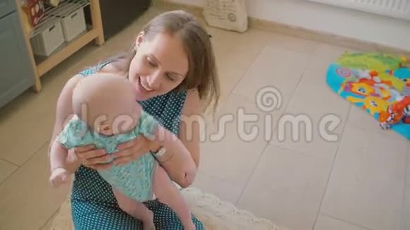 年轻的母亲抱着她的宝贝微笑着看着他坐在厨房的地板上慢动作视频的预览图