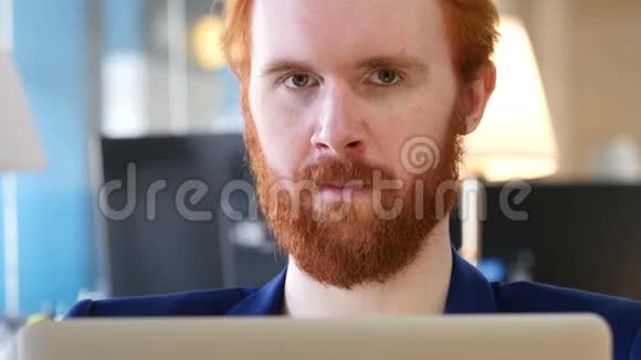 戴红发的男人朝办公室的摄像头微笑视频的预览图