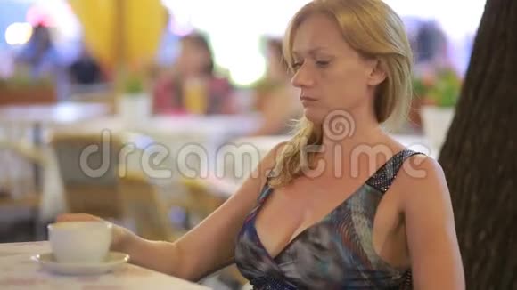 年轻漂亮的金发女人晚上坐在咖啡馆里视频的预览图