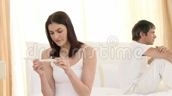女人看着怀孕测试愤怒的男人坐在床上视频的预览图