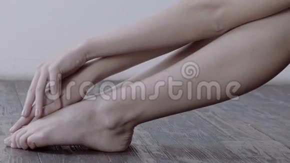 女人轻轻地摸着她的腿坐在木地板上背景是白色的墙视频的预览图