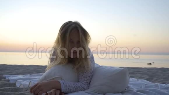 那个女孩躺在沙滩上枕头和毯子之间日落浪漫慢动作特写美丽的视频的预览图
