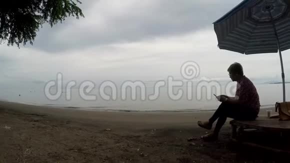 成熟女性盘腿坐在遮阳伞下用手机上网视频的预览图
