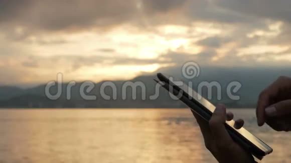 日出时分一个男人在海边查看平板电脑上的信息绚丽的天空和朝阳视频的预览图