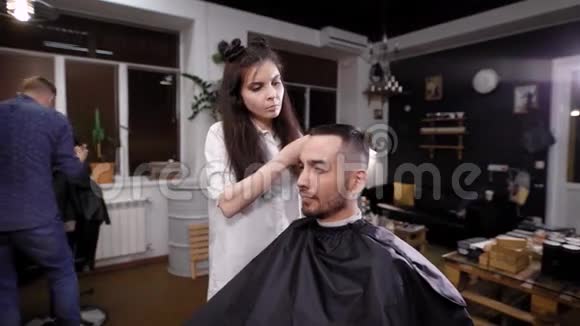 年轻的女理发师在沙龙里给男人做时髦的头发视频的预览图