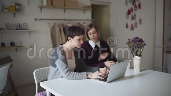 两个年轻的女人坐在桌子上用笔记本在电脑上工作的女人视频的预览图