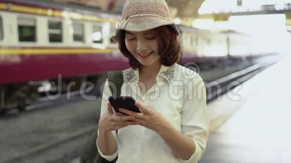 快乐的年轻女性在火车站用智能手机聊天阅读和发短信视频的预览图