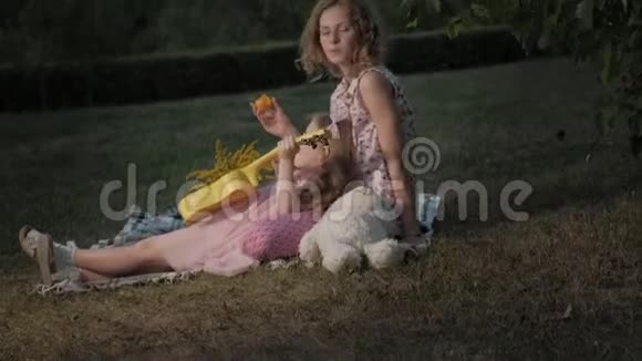 一对幸福的母女正在玩四弦琴一家人在城市公园里在日落的温暖的晚上野餐视频的预览图