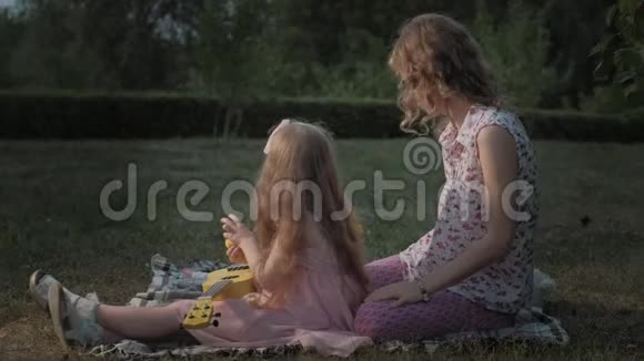 一对幸福的母女正在玩四弦琴一家人在城市公园里在日落的温暖的晚上野餐视频的预览图