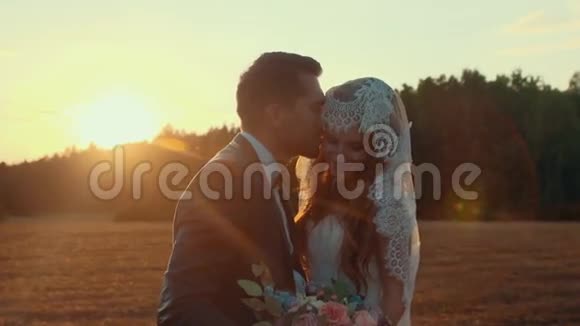 在夕阳西下的夏日新婚夫妇在田野里拥抱和亲吻视频的预览图