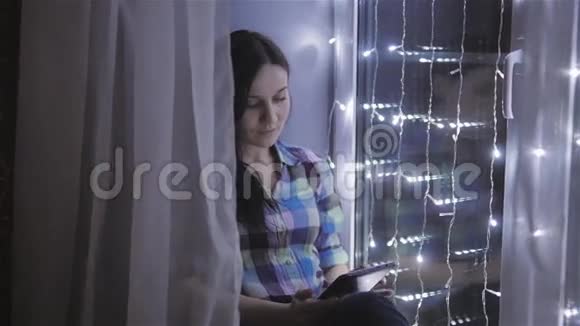 美丽迷人的女人使用平板电脑和坐在窗前装饰着花环视频的预览图