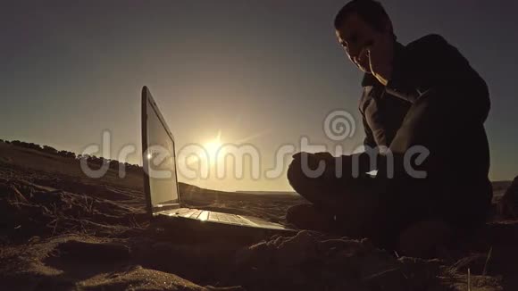 一个商人自由职业者打着电话坐在沙滩上后面坐在沙滩上在阳光下自由职业者的剪影里视频的预览图