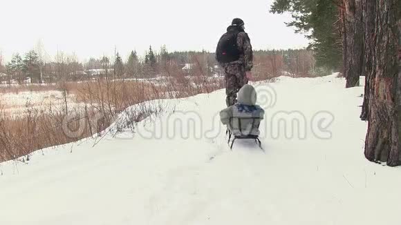 父亲带着孩子在雪橇上穿过树林视频的预览图