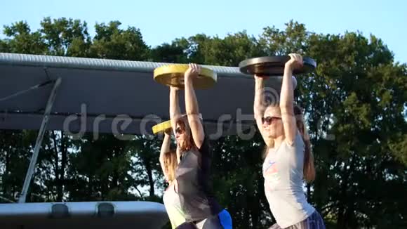 日落时分运动型的年轻女性戴着太阳镜穿着紧身衣在体重重量重的盘子上做运动视频的预览图
