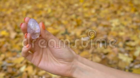 带橙色指甲的女性手拿着透明紫罗兰紫水晶玉尼蛋用于Vumfit冥想视频的预览图