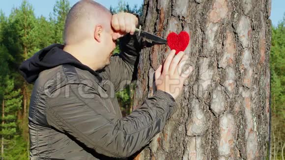 愁眉苦脸的人拿着刀把心织在树旁视频的预览图