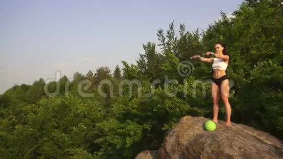 适合黑发女人做户外哑铃运动在山峰上训练青山绿水视频的预览图