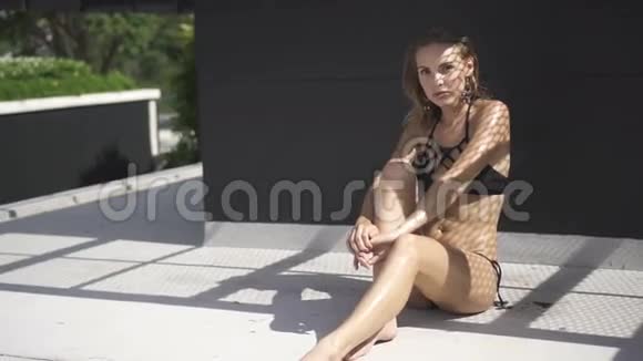 美丽的金发女人穿着黑色泳装坐在屋顶上在一个阳光明媚的夏天阴影网反射视频的预览图