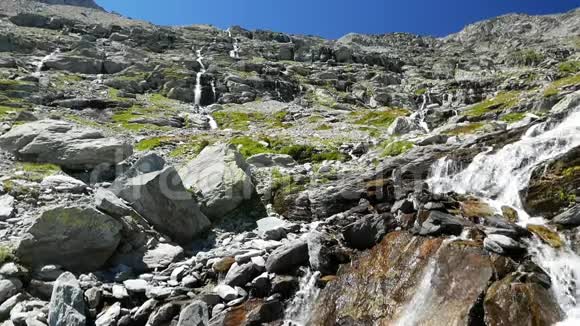 瀑布在田园诗般的无污染环境中流动夏天穿过阿尔卑斯山上的绿色草地和巨石视频的预览图