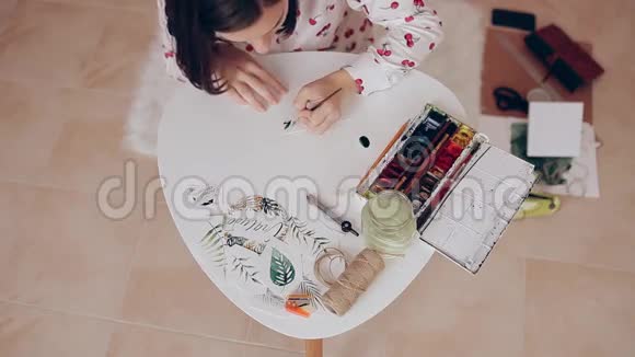 女孩用画笔和水彩画在纸上手工制作的节日装饰品视频的预览图