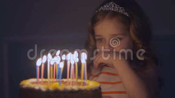 一个小女孩看着节日蛋糕上的蜡烛慢慢地许愿视频的预览图