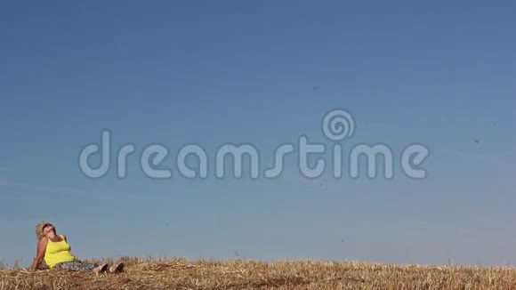 女人坐在田野里戴着太阳镜看着天空阳光明媚的天气视频的预览图