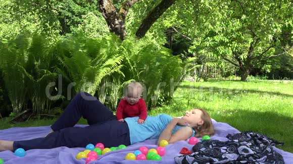 快乐的母亲躺在格子布上在夏天的公园里小女儿躺在格子布上4K视频的预览图