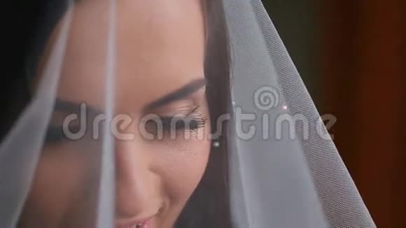 年轻美丽的新娘在白色婚纱下的脸视频的预览图