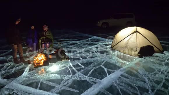 晚上有四个旅行者乘火在冰上在冰上露营帐篷就在火旁边周围的人都在变暖视频的预览图