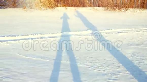 浪漫情侣在日落时分的冬日阳光明媚的雪地上徒步旅行的影子3840x2160视频的预览图