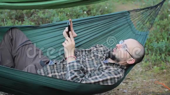 一个吊床上的男人在打电话一个留着胡子戴眼镜的人视频的预览图
