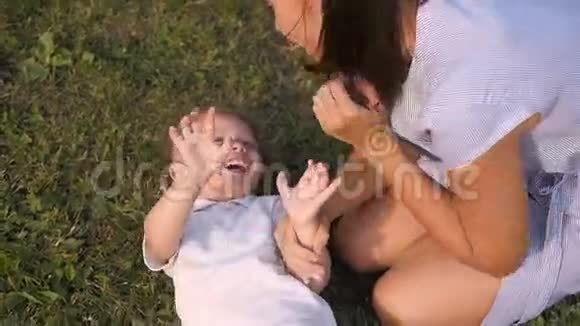 母亲和她的儿子在公园的草地上玩妈妈在挠痒痒和亲吻儿子视频的预览图