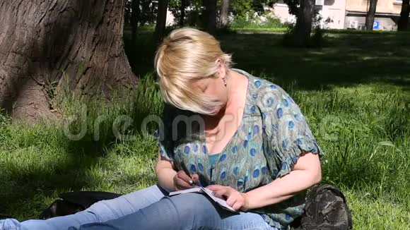 妇女和学生坐在草地上在笔记本上做笔记学习和写思想写书视频的预览图