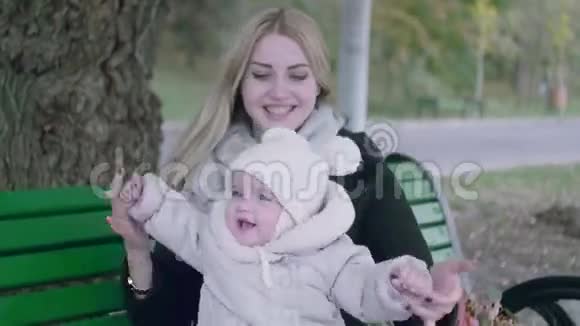 美丽的年轻妈妈和她可爱的小宝宝在秋天公园的长凳上玩耍视频的预览图