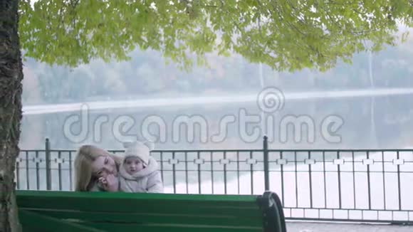 美丽的年轻妈妈和她可爱的小宝宝在秋天公园的长凳上玩耍视频的预览图