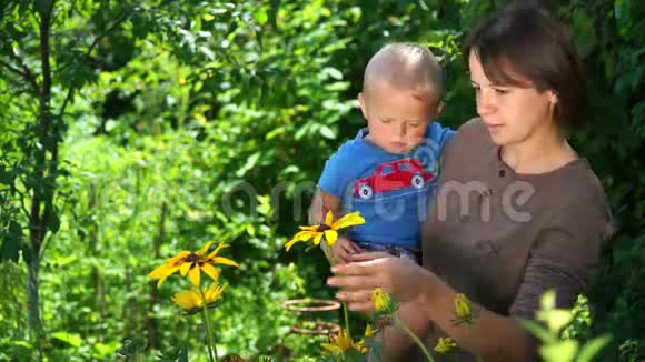 可爱的年轻母亲和一个小儿子在花园里闻花视频的预览图