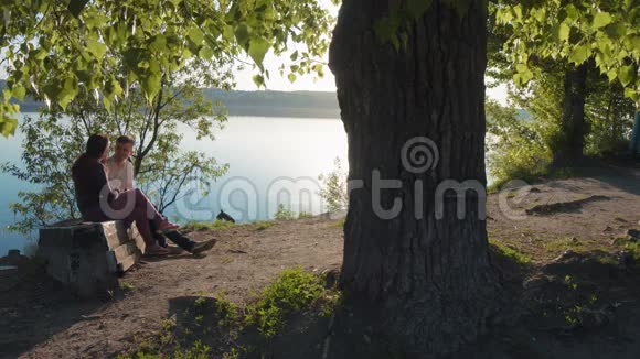 美丽的女孩和一个坐在河边的男人视频的预览图