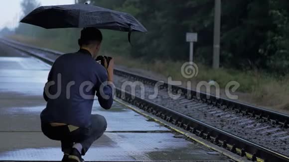 年轻人摄影师用雨伞在雨中拍照视频的预览图