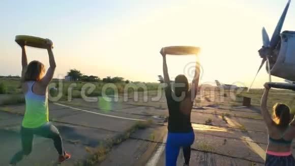 日落时分运动型的年轻女性戴着太阳镜穿着紧身衣在体重重量重的盘子上做运动视频的预览图