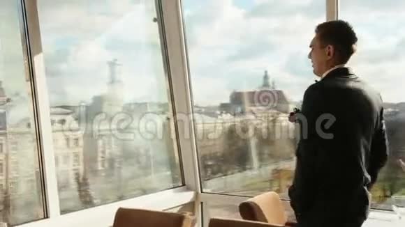 英俊自信的男人穿着黑色西装站在咖啡馆的玻璃墙上令人惊叹的Lviv场景背景视频的预览图