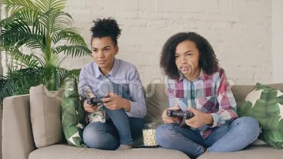 两个混血卷毛的女孩朋友坐在沙发上玩游戏控制台电脑游戏在家玩得很开心视频的预览图