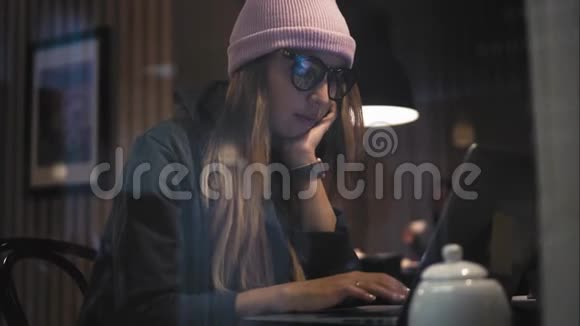 一个穿眼镜的时髦女孩在笔记本电脑上打字从窗口观看视频的预览图