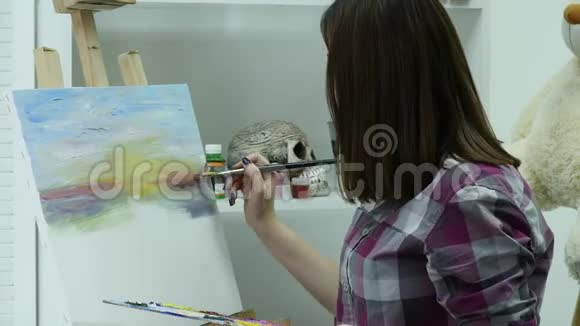 艺术家在画布上画一个女人并涂上一层宽的画笔帆布站在画架上画家在画架上画画视频的预览图
