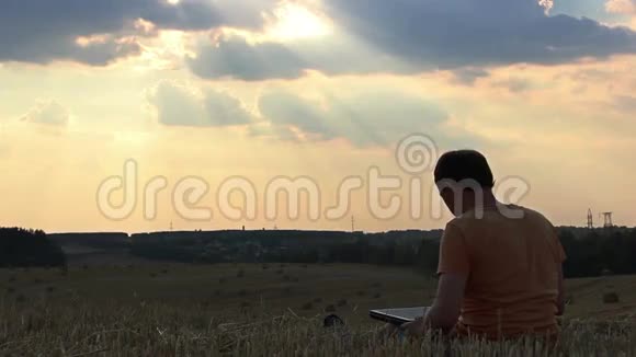 日落时分一个人带着笔记本电脑在田野里一个人在日落时分在上面工作视频的预览图