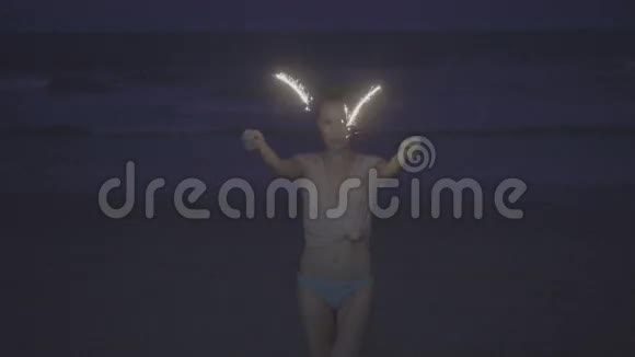 晚上在海滩上用闪闪发光的烟花特写性感女人视频的预览图