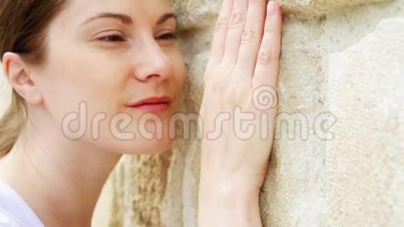 女人用手缓慢地靠在老石墙上女性触摸粗糙的岩石表面视频的预览图