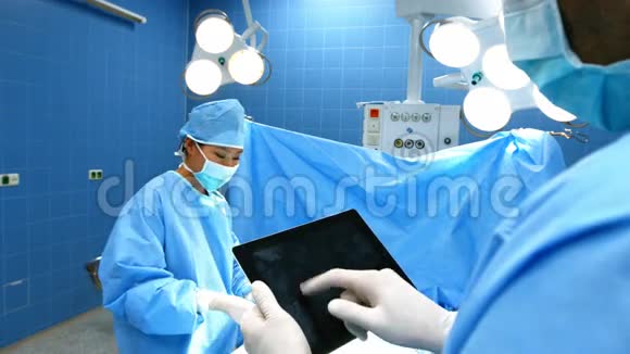 外科医生使用数码平板电脑同事在手术室操作病人视频的预览图