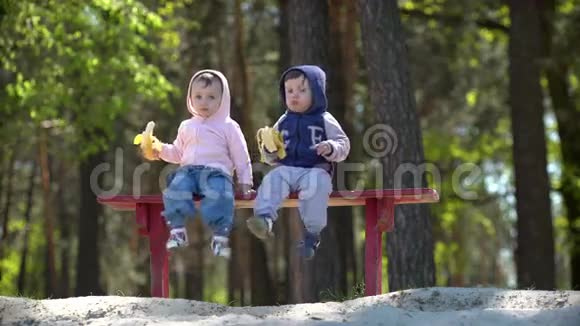 坐在长凳上吃香蕉的两个小孩子视频的预览图