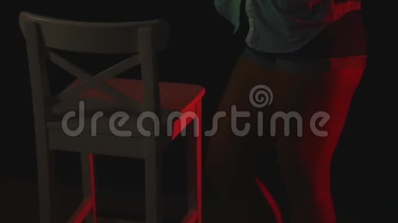 穿着短短裤和一件衬衫在黑暗的椅子上跳舞视频的预览图