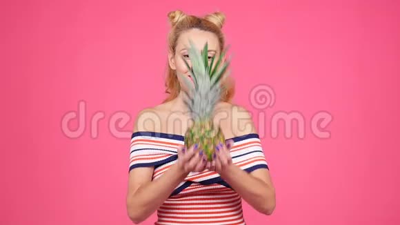 一位年轻女子在粉色背景上拿着菠萝视频的预览图